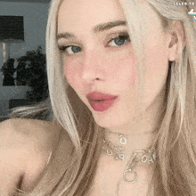 a close up of a blonde woman wearing a necklace with the letter c on it