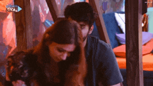 a man and a woman are hugging in front of a sign that says 24hr live channel .