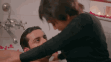 a woman is putting her hand on a man 's face in a bathtub filled with rose petals .