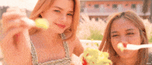 two young women are standing next to each other and eating a salad .