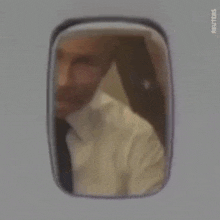 a man in a suit and tie is looking out of a window of an airplane .