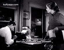 a man is sitting at a desk with a typewriter and a woman is standing next to him and talking to him .
