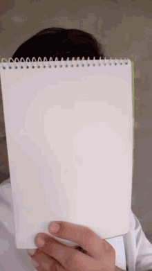 a person covering their face with a spiral bound notebook
