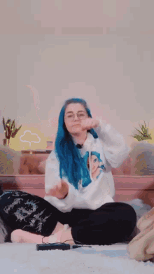 a girl with blue hair and glasses sits on the floor