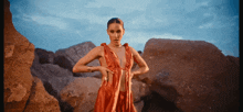 a woman in a red dress stands in front of a pile of rocks