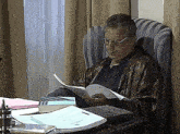 a man wearing glasses is sitting at a desk reading a book