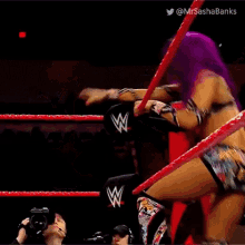 a referee is standing in the middle of a wrestling ring while a wrestler is falling through the ropes .
