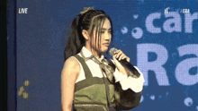 a woman is singing into a microphone in front of a screen that says " live "