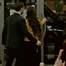 a man in a suit and a woman in a yellow sweater are entering a store