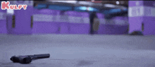 a gun is laying on the ground in front of a purple wall in a parking garage .
