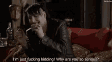 a man is sitting on a couch talking to another man and says i 'm just fucking kidding