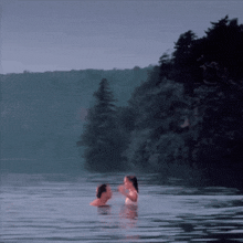 a man and a woman are swimming in a lake with trees in the background