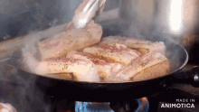 bacon is being cooked in a pan on a stove with tongs