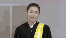 a woman in a graduation gown with a yellow sash smiles for the camera