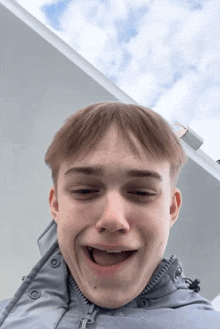 a young man wearing a grey jacket has his tongue hanging out