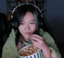 a woman wearing headphones is eating a bowl of popcorn with a straw