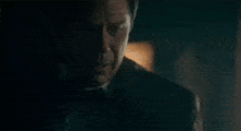 a man in a black coat is standing in a dark room talking to a woman .