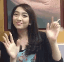 a woman is waving her hands in front of a painting of a woman 's face