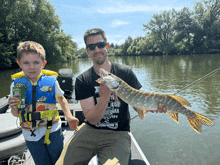 a man holding a large fish next to a boy in a life jacket