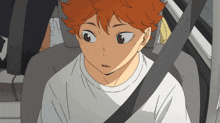 a boy with orange hair is sitting in a car with a seat belt on