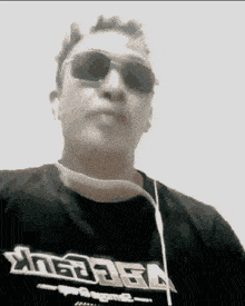 a man wearing sunglasses and a t-shirt that says ' xtreme ' on it looks at the camera