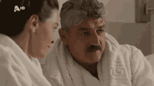 a man with a mustache is talking to a woman in a bathrobe with a hd logo on the bottom