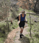 a woman in a blue tank top and black shorts walks down a dirt path