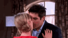 a man and woman are kissing in front of a window .