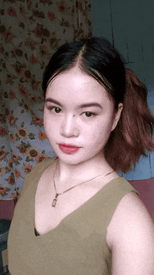 a woman wearing a green tank top and a gold necklace with a pendant on it