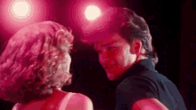 a man and a woman are dancing together in a dark room with pink lights .