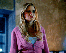 a blonde woman wearing a pink cardigan is standing in a room