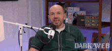 a man in a green shirt is sitting in front of a microphone with the words dark web written on the bottom .