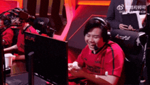 a man wearing headphones and a red shirt that says autofull laughs in front of a computer monitor