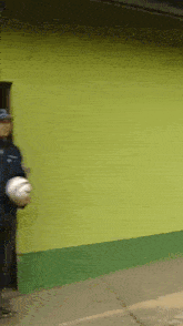 a man in a blue jacket is holding a white ball in front of a green wall