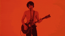a man playing a guitar and singing into a microphone with a red background