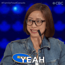 a woman wearing glasses and a denim jacket says " yeah " in front of a microphone