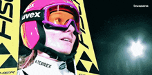a woman wearing a pink helmet and goggles with uvex on it