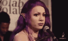 a woman with purple hair is singing into a microphone while wearing elf ears .