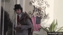 a man in a hat and tie is standing in front of an american flag in a room .