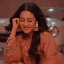 a woman in a pink dress and earrings is sitting in front of a car .
