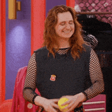 a woman wearing a black tank top and fishnet sleeves is smiling while holding a yellow ball
