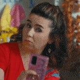 a woman in a red shirt is holding a cell phone in her hand
