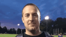 a man in a black shirt is standing in front of a field at night