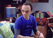 a man in a blue shirt with superman on it is sitting on a couch