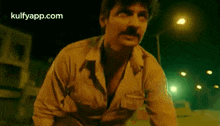 a man with a mustache is standing in front of a building at night .