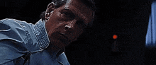 a man in a blue shirt is looking at the camera in a dark room