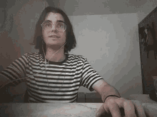 a young man wearing a striped shirt and glasses looks at the camera