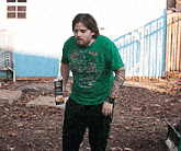 a man in a green shirt is holding a bottle of beer