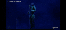 a man in a green suit is standing in front of a blue background with the words tyler the creator on the bottom