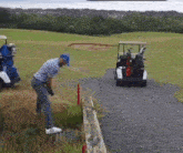 a man is swinging a golf club on a golf course while a golf cart is driving by .